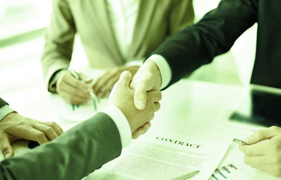 Business meeting shaking hands and signing paperwork at a table