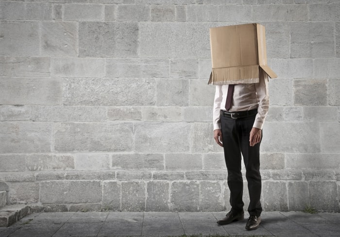 A man with a suit standing in front of a grey brick background with a box over his head.  4 types of attendees at a trade show.