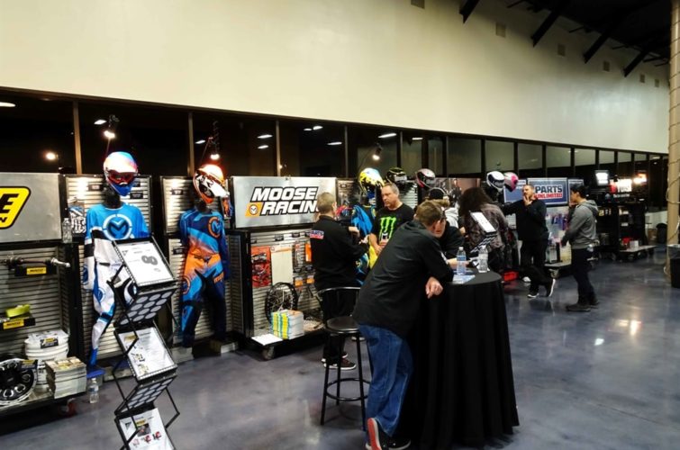 people talking in front of the exhibition for motorcycle suits and equipment at Super Show Expo