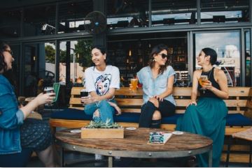 Four female friends drinking coffee and tea outside of a coffee shop. 
