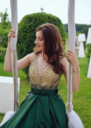 Woman at a wedding on a swing wearing a formal dress that is beige and green. 